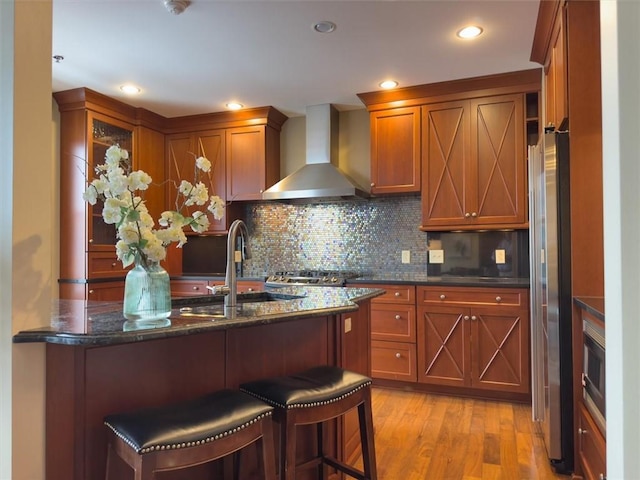 kitchen featuring appliances with stainless steel finishes, light hardwood / wood-style floors, wall chimney exhaust hood, sink, and backsplash