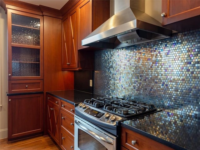 kitchen with stainless steel range with gas stovetop, island exhaust hood, light wood-type flooring, dark stone counters, and tasteful backsplash