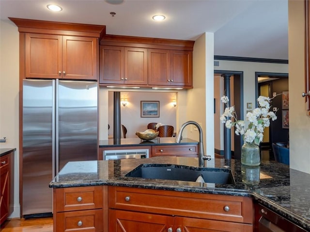 kitchen featuring stainless steel appliances, light hardwood / wood-style floors, dark stone counters, ornamental molding, and sink