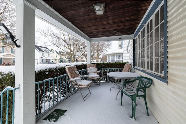 snow covered back of property featuring covered porch