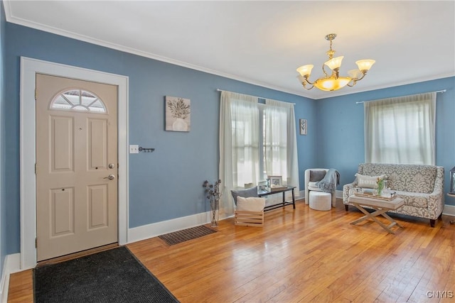 entrance foyer featuring hardwood / wood-style flooring, an inviting chandelier, a wealth of natural light, and crown molding