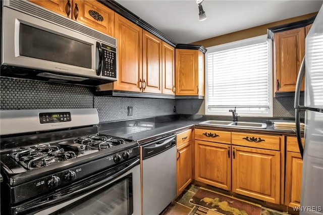 kitchen with rail lighting, appliances with stainless steel finishes, dark tile patterned floors, sink, and backsplash