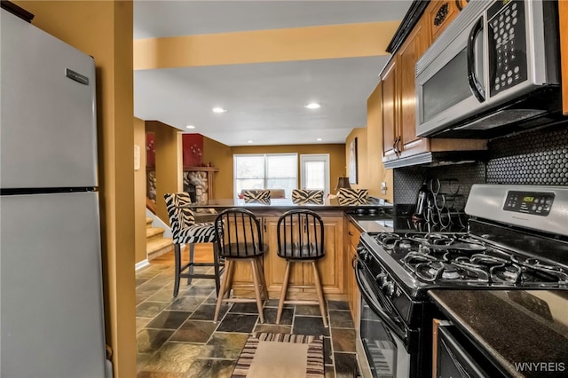 kitchen with stainless steel appliances, kitchen peninsula, a kitchen bar, and tasteful backsplash