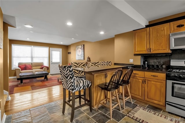 kitchen featuring kitchen peninsula, stainless steel range with gas cooktop, tasteful backsplash, and a kitchen bar