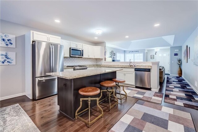 kitchen featuring appliances with stainless steel finishes, white cabinetry, backsplash, kitchen peninsula, and a breakfast bar