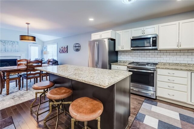 kitchen with a breakfast bar, decorative backsplash, hanging light fixtures, stainless steel appliances, and white cabinets