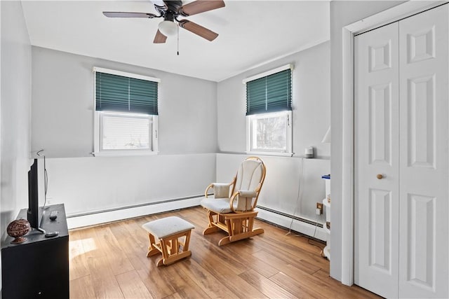 living area featuring wood-type flooring, a baseboard radiator, and ceiling fan