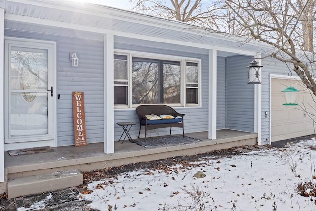 snow covered property entrance with covered porch and a garage