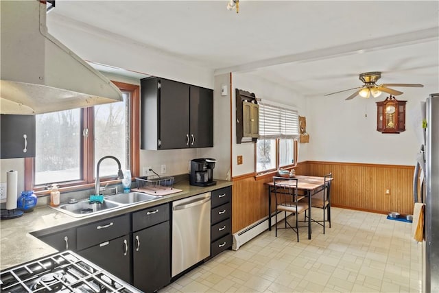 kitchen featuring wood walls, appliances with stainless steel finishes, ceiling fan, a baseboard heating unit, and sink