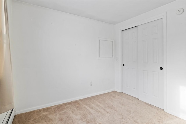 unfurnished bedroom featuring light colored carpet, a closet, and a baseboard heating unit