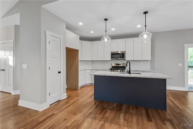 kitchen featuring hanging light fixtures, stainless steel appliances, an island with sink, tasteful backsplash, and white cabinetry