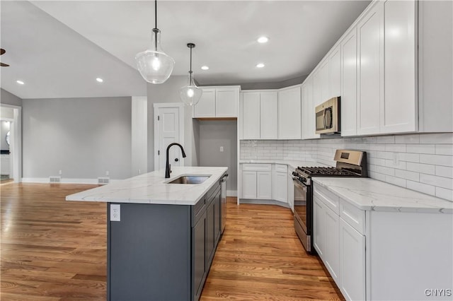 kitchen featuring a center island with sink, stainless steel appliances, hanging light fixtures, sink, and white cabinetry