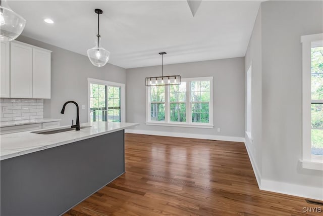 kitchen with light stone countertops, hanging light fixtures, tasteful backsplash, white cabinetry, and sink