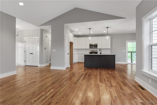 kitchen with decorative light fixtures, an island with sink, tasteful backsplash, white cabinetry, and appliances with stainless steel finishes