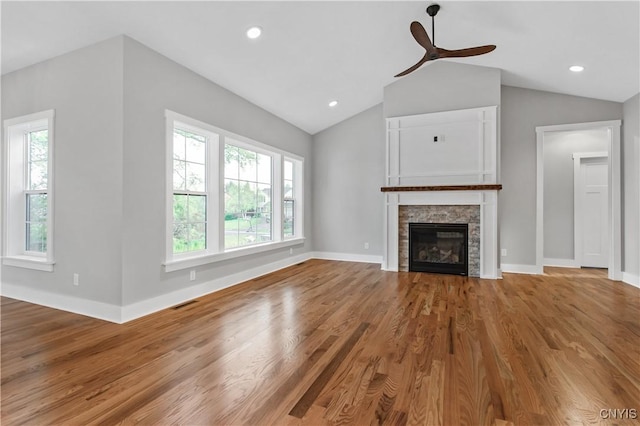 unfurnished living room with lofted ceiling, a healthy amount of sunlight, hardwood / wood-style flooring, and a stone fireplace