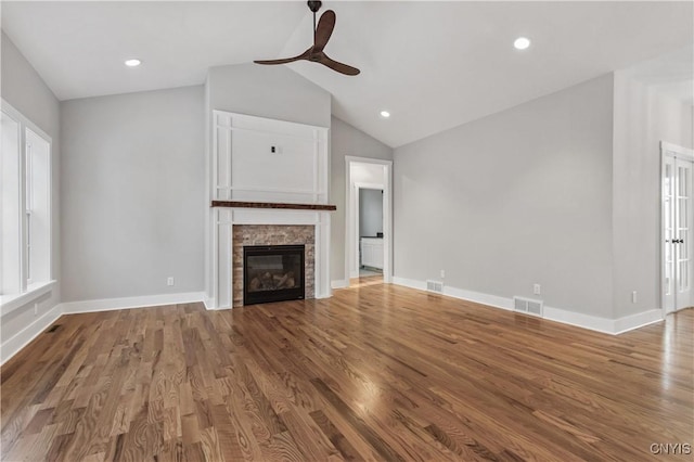 unfurnished living room featuring ceiling fan, a stone fireplace, lofted ceiling, and wood-type flooring