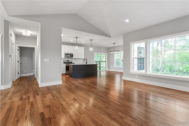 unfurnished living room with lofted ceiling, dark hardwood / wood-style flooring, sink, and a healthy amount of sunlight