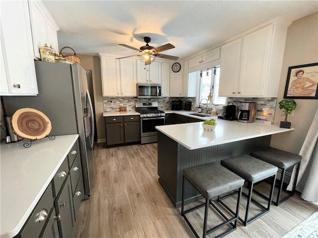 kitchen featuring a kitchen breakfast bar, stainless steel appliances, gray cabinetry, and white cabinets