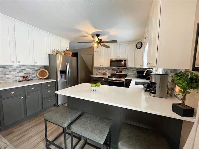 kitchen with kitchen peninsula, sink, gray cabinetry, stainless steel appliances, and white cabinets