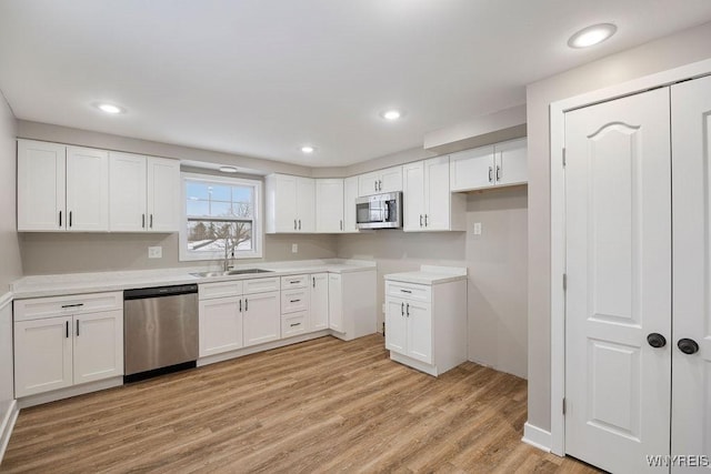 kitchen featuring light wood-type flooring, appliances with stainless steel finishes, white cabinetry, and sink