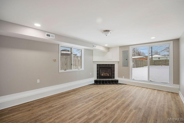 unfurnished living room featuring light hardwood / wood-style floors, a tile fireplace, and electric panel