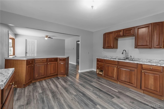 kitchen with sink, light stone counters, ceiling fan, kitchen peninsula, and dark wood-type flooring