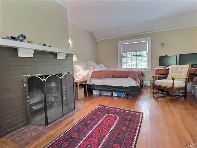 bedroom featuring vaulted ceiling, a fireplace, and wood-type flooring