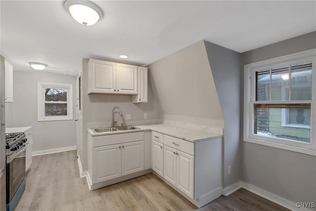 kitchen with white cabinets, stainless steel gas stove, light hardwood / wood-style flooring, and sink