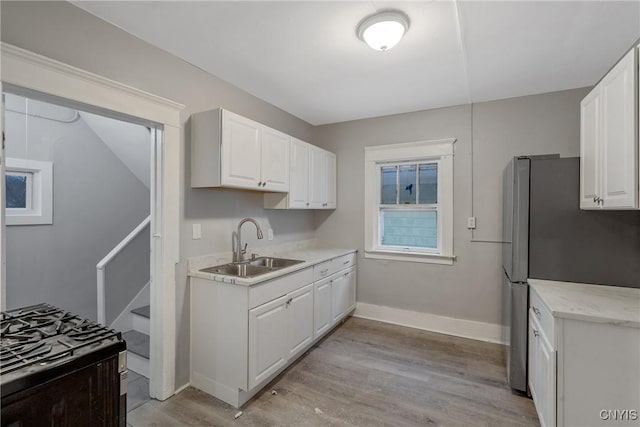 kitchen with stainless steel refrigerator, white cabinets, light hardwood / wood-style flooring, and sink