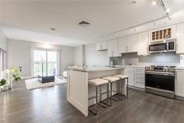 kitchen with a breakfast bar, a kitchen island, backsplash, white cabinets, and appliances with stainless steel finishes