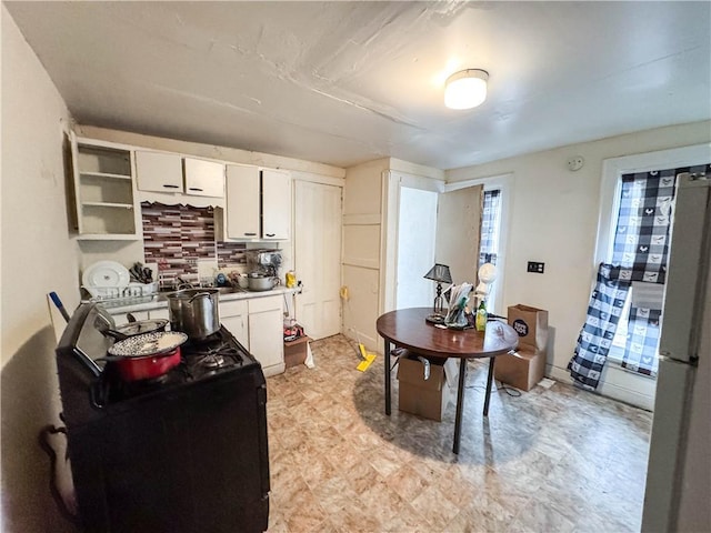 kitchen featuring white cabinets, white fridge, tasteful backsplash, and black range