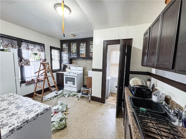 kitchen featuring white appliances, light stone counters, dark brown cabinets, and sink