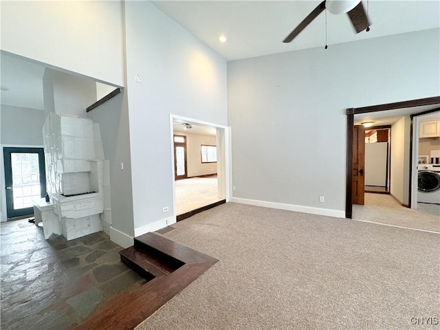 unfurnished living room with a healthy amount of sunlight, a high ceiling, washer / dryer, ceiling fan, and light carpet