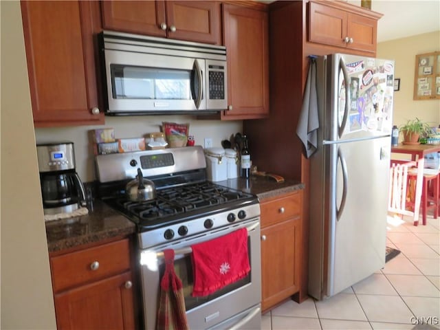 kitchen featuring stainless steel appliances, light tile patterned floors, and dark stone counters