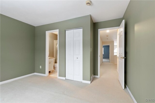 unfurnished bedroom with ensuite bath, a closet, and light colored carpet