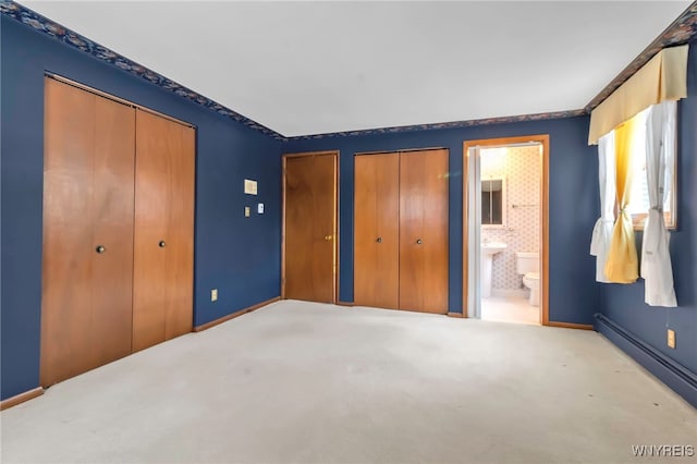 unfurnished bedroom with a baseboard heating unit, two closets, light colored carpet, and ensuite bath