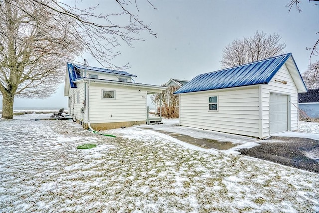 snow covered rear of property with a garage and an outdoor structure