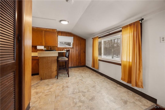 kitchen featuring a breakfast bar, wooden walls, vaulted ceiling, and kitchen peninsula