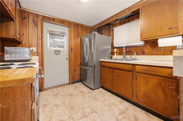 kitchen featuring sink, stainless steel fridge, wooden walls, and electric stove