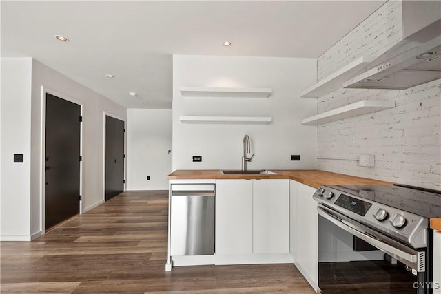 kitchen with white cabinetry, wooden counters, stainless steel appliances, wall chimney range hood, and sink