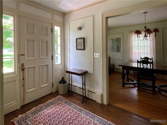 foyer entrance with dark wood-type flooring, a baseboard radiator, crown molding, and a chandelier