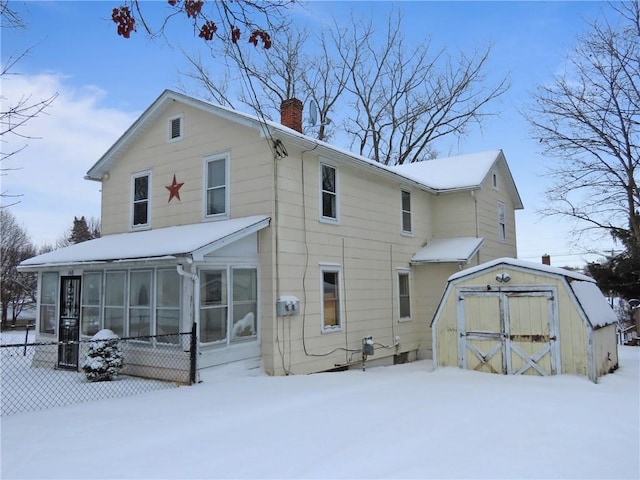 snow covered property with a sunroom and a storage shed