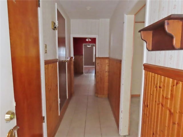 hallway featuring wooden walls and light tile patterned flooring