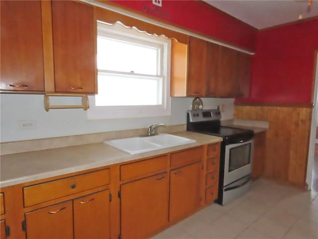 kitchen with stainless steel electric range, light tile patterned floors, wooden walls, and sink