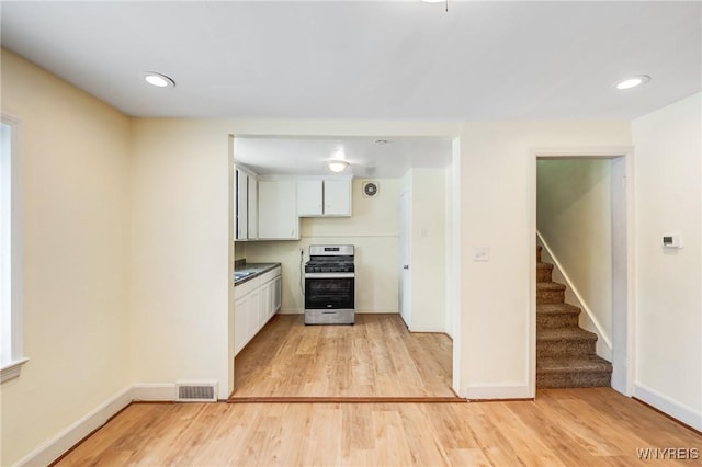 kitchen with white cabinets, stainless steel gas range oven, and light hardwood / wood-style flooring