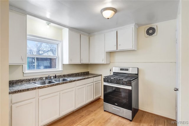 kitchen featuring sink, stainless steel gas stove, white cabinets, and light wood-type flooring