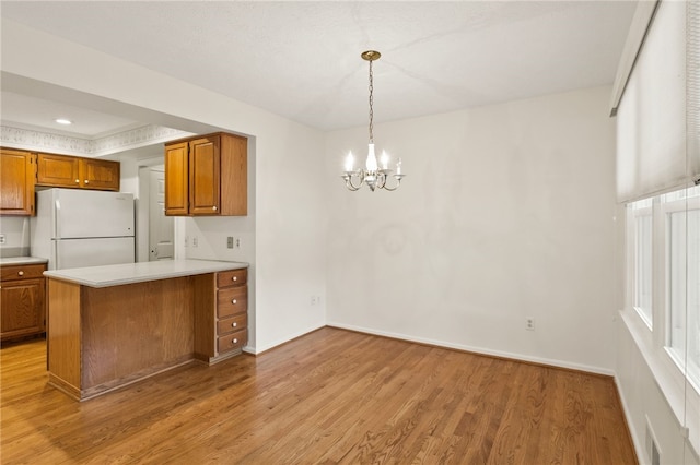 kitchen with kitchen peninsula, pendant lighting, white fridge, a notable chandelier, and light wood-type flooring