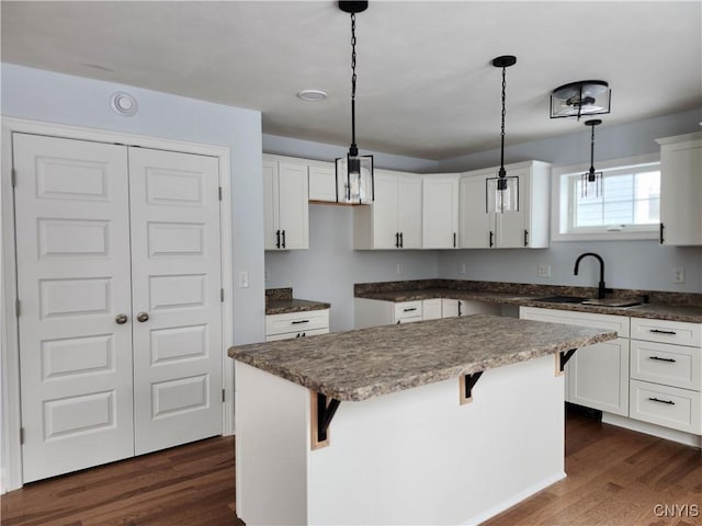 kitchen featuring hanging light fixtures, a breakfast bar, a kitchen island, white cabinets, and sink