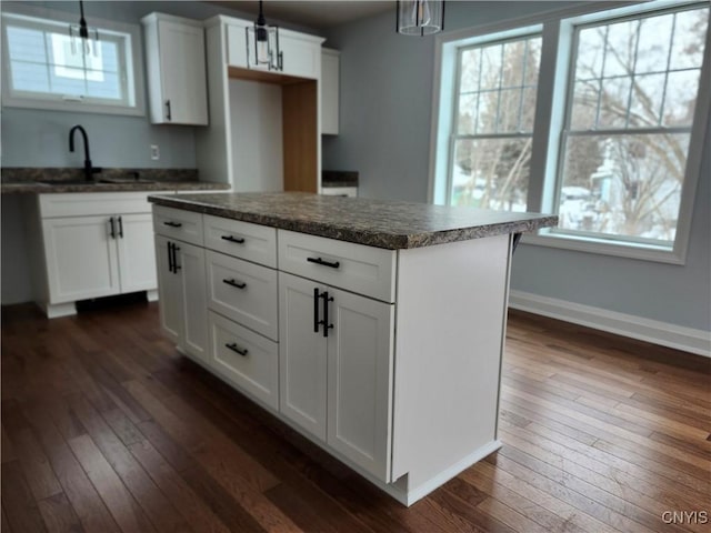 kitchen featuring pendant lighting, dark hardwood / wood-style floors, a kitchen island, white cabinets, and sink