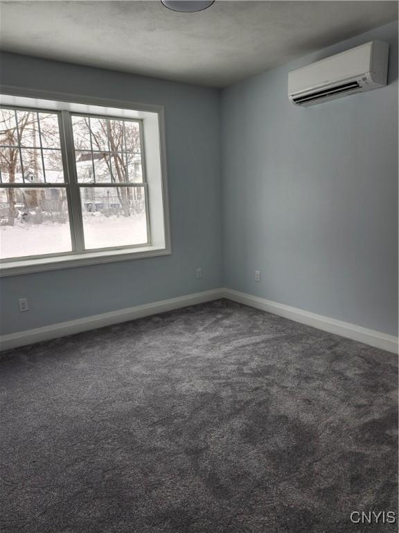 unfurnished room with a wall mounted air conditioner and dark colored carpet